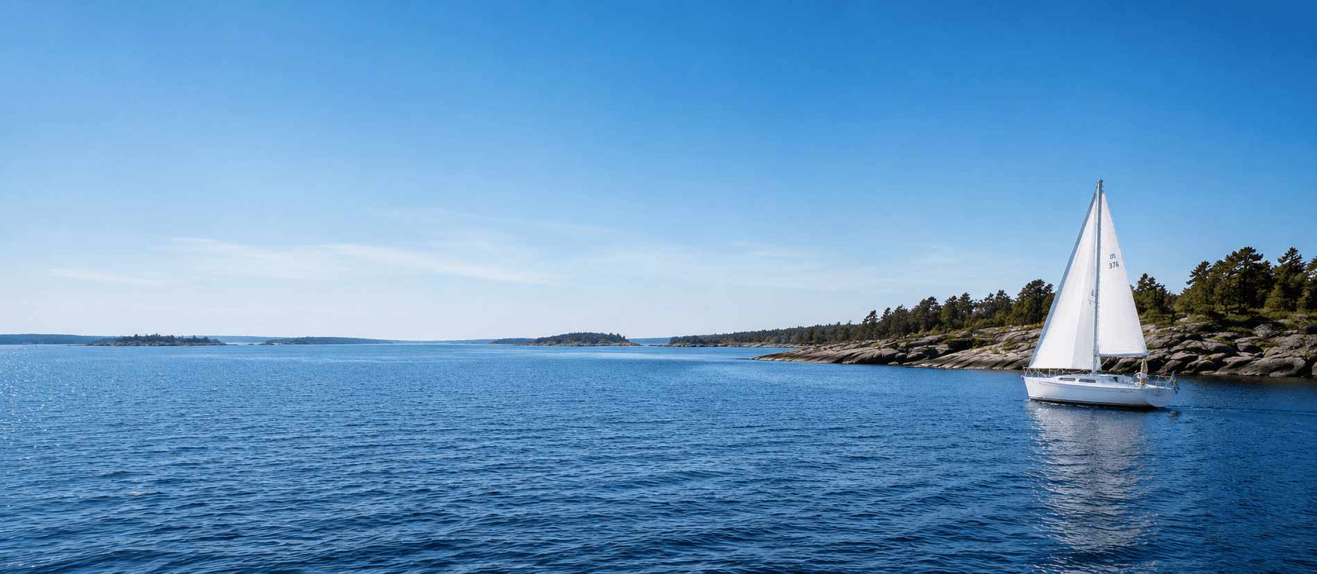 Vidblick över svenska skärgården med blått vatten, klippöar och en segelbåt långt till höger
